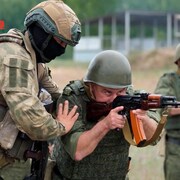 Un militaire aide un soldat qui regarde dans le viseur d'un fusil.