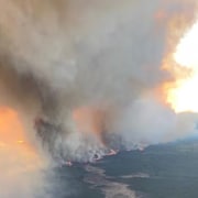 Une photo prise d'un avion montre un grand feu de forêt qui brûle au sol avec beaucoup de fumée. 