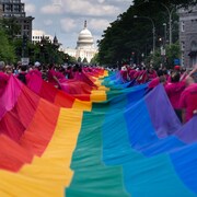 Des gens portent une immense banderole arc-en-ciel.