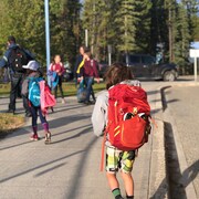 Un enfant avec un sac à dos sort d'un autobus scolaire et se dirige vers d'autres enfants.