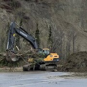 Un engin de chantier retire des débris d'un glissement de terrain sur une route.