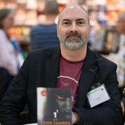 L’auteur Yvan Godbout photographié lors d’un salon du livre. On aperçoit, à l’avant-plan, une copie de son roman «Les Yeux jaunes».
