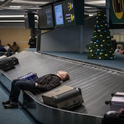 Un passager se repose sur le carrousel à bagages à l'aéroport de Vancouver à la suite de l'annulation d'une cinquantaine de vols le 20 décembre 2022.