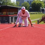 En habit de baseball des Diamants, de face, il prend sa position de d&eacute;part sur la piste d'athl&eacute;tisme.