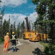 Des travailleurs regardent une foreuse minière dans la forêt.
