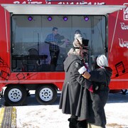 Un couple danse devant un camion dans lequel il y a deux violonistes. 