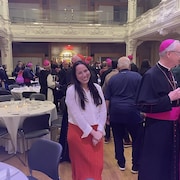 La femme pose pour la caméra au milieu d'une grande salle remplie de personnes en habit religieux.