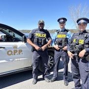 Deux membres de la police provinciale et un jeune homme bénévole en uniforme devant une voiture de la Police provinciale de l'Ontario.