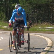 Shelley Gautier est sur un vélo et sur le bord de la route, son conjoint Alan Geer tient un drapeau du Canada. 