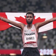Le coureur tient le drapeau canadien derrière son dos.