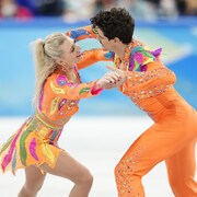 Les deux danseurs se regardent dans les yeux et se tiennent les mains sur la glace.