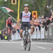 Adam Yates, en blanc et noir, crie de joie alors qu'il traverse seul le fil d'arrivée à la fin de la course.