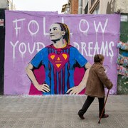 Une femme marche avec une canne devant une peinture murale représentant une joueuse de soccer espagnole.