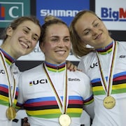 Trois cyclistes sourient sur le podium, chacune avec une médaille d'or au cou. 