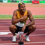 Un coureur est accroupi sur une piste d'athlétisme et pose avec un trophée de la Diamond League.