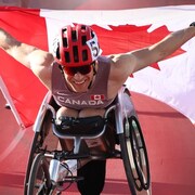 L'homme en fauteuil roulant tient le drapeau canadien derrière lui.