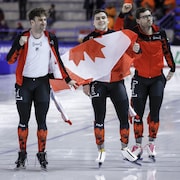 Trois patineurs canadiens célèbrent leur triomphe sur la glace.
