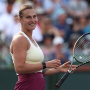 Une joueuse de tennis tient sa raquette dans une main et sourit après avoir remporté un match.