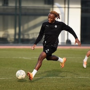 Un joueur de soccer, habillé tout en noir, s'apprête à frapper le ballon pendant un entraînement. 