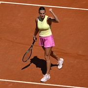 Une joueuse de tennis regarde à sa gauche, lève la main gauche et serre le poing sur un court en terre battue.  