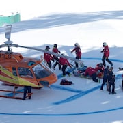 Des secouristes entourent un skieur couché au sol, tout près d'un hélicoptère de secours.