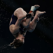 Une athlète de plongeon agrippe ses jambes durant un saut périlleux.