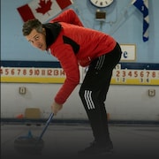 Un homme balaie la glace devant une pierre de curling.