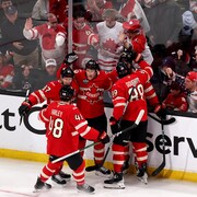 Des joueurs de hockey célèbrent sur la glace, devant des spectateurs. 