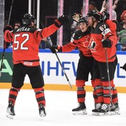 Trois joueurs de hockey du Canada se prennent dans les bras pour célébrer un but.