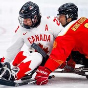 Un joueur de l'équipe canadienne de parahockey contrôle la rondelle devant un adversaire de la Chine.