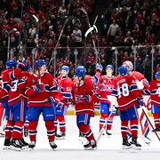 Réunis au centre de la patinoire, les joueurs du Canadien sourient et lèvent leur bâton.
