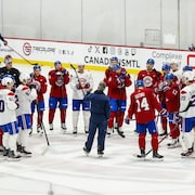 Des joueurs de hockey regroup&eacute;s en cercle sur la glace &eacute;coutent l'entra&icirc;neur parler, qui est situ&eacute; au centre du groupe.