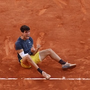 Carlos Alcaraz, assis au sol, brandit les poings pour célébrer sa victoire en finale du tournoi de Roland-Garros, à Paris, contre Alexander Zverev.