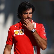 Un pilote de F1 marche, la main gauche sur son visage. 