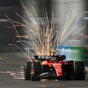 Une monoplace de Ferrari roule sur un circuit éclairé et fait des étincelles.