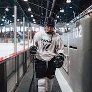 Une joueuse de hockey vêtue d'un chandail blanc sort de la patinoire. 