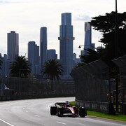 Une voiture de course en piste avec la ville de Melbourne en arrière plan.