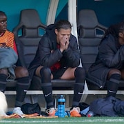 Assise sur le banc de son équipe, une joueuse de soccer porte les mains à son visage.