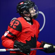 Une joueuse de hockey, de profil et casquée, marche la tête haute, son bâton bien en main.  