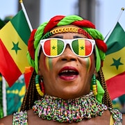 Une femme arborant des drapeaux du Sénégal et des lunettes aux couleurs du drapeau regarde au loin.