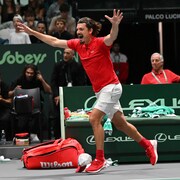 Un entraîneur de tennis, vêtu de rouge et blanc, court vers le terrain les bras dans les airs après la victoire de son équipe. 