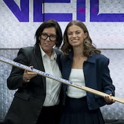 Deux femmes en veston posent avec un bâton de hockey dans les mains.