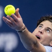 Un joueur de tennis lance la balle. 