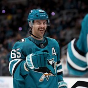 Un joueur de hockey, à l'uniforme turquoise, sourit en offrant le poing. 