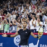 Un joueur de tennis se tient les bras en croix après avoir remporté une manche.