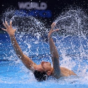Un homme tend ses bras pendant une compétition de natation artistique dans une piscine.