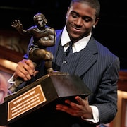 Un homme souriant regarde et tient un trophée à l'effigie d'un joueur de football.