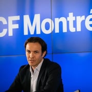 Un homme en complet devant un fond bleu sur lequel on peut lire : CF Montréal