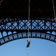 Suspendue à la tour Eiffel, elle s'accroche à une corde et regarde vers le haut.