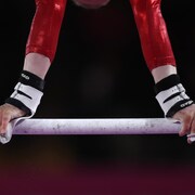 Une athlète se tient avec ses bras, tête à l'envers, sur une barre horizontale.